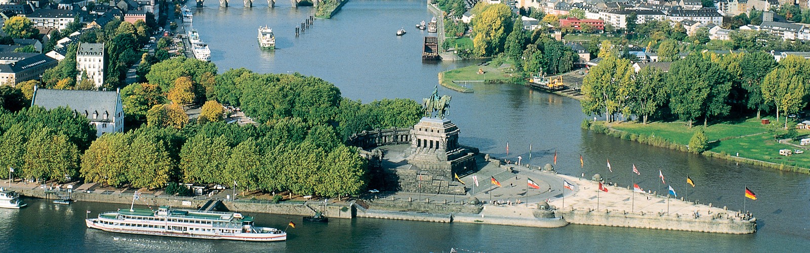 Drone shot of the city, featuring a body of water and a large sculpture of a solider on the land.